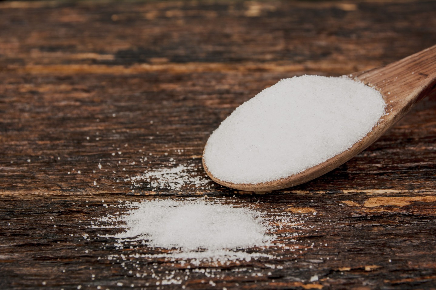 Sugar on a wooden spoon on wooden table