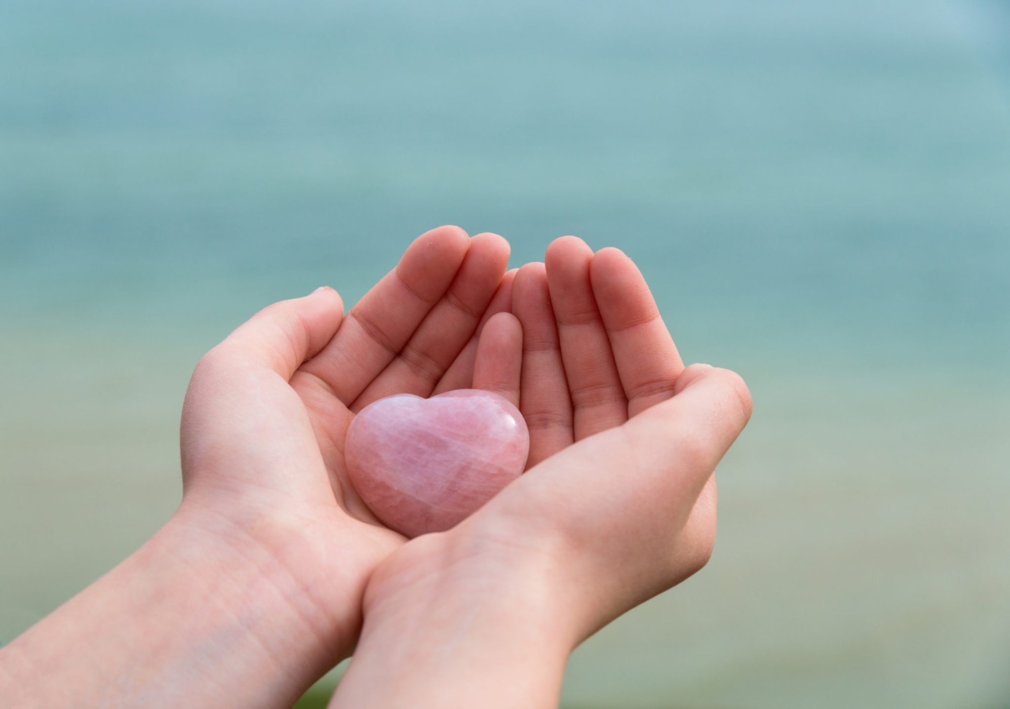 Stone heart in child's hands against blue sea