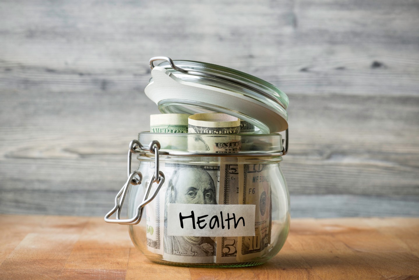 Dollar bills in glass jar isolated on wooden background. Saving money for health.
