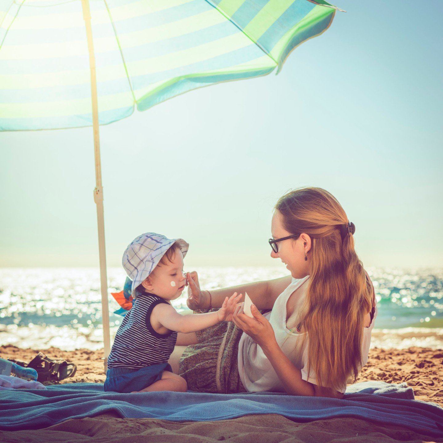 Young mother applying sunblock cream on her baby boy at the beach||sun safety tips