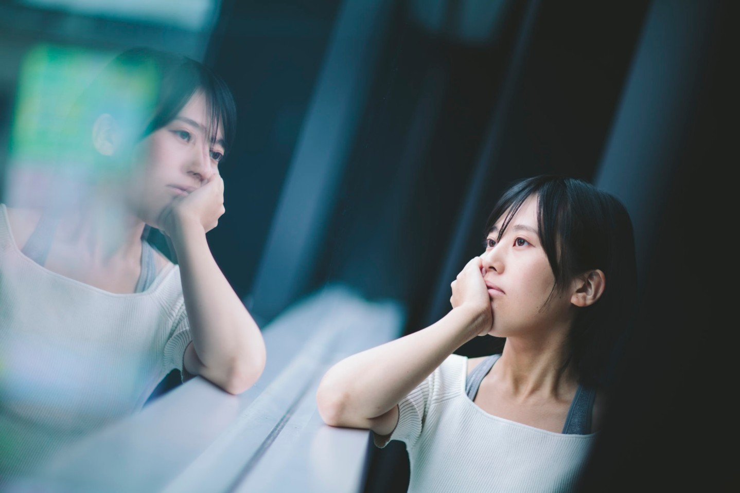 A young woman is looking outside through the window and thinking something deeply alone.