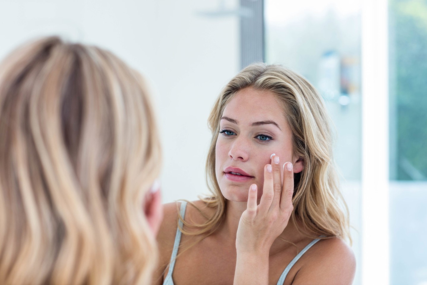woman-applying-sunscreen-mirror