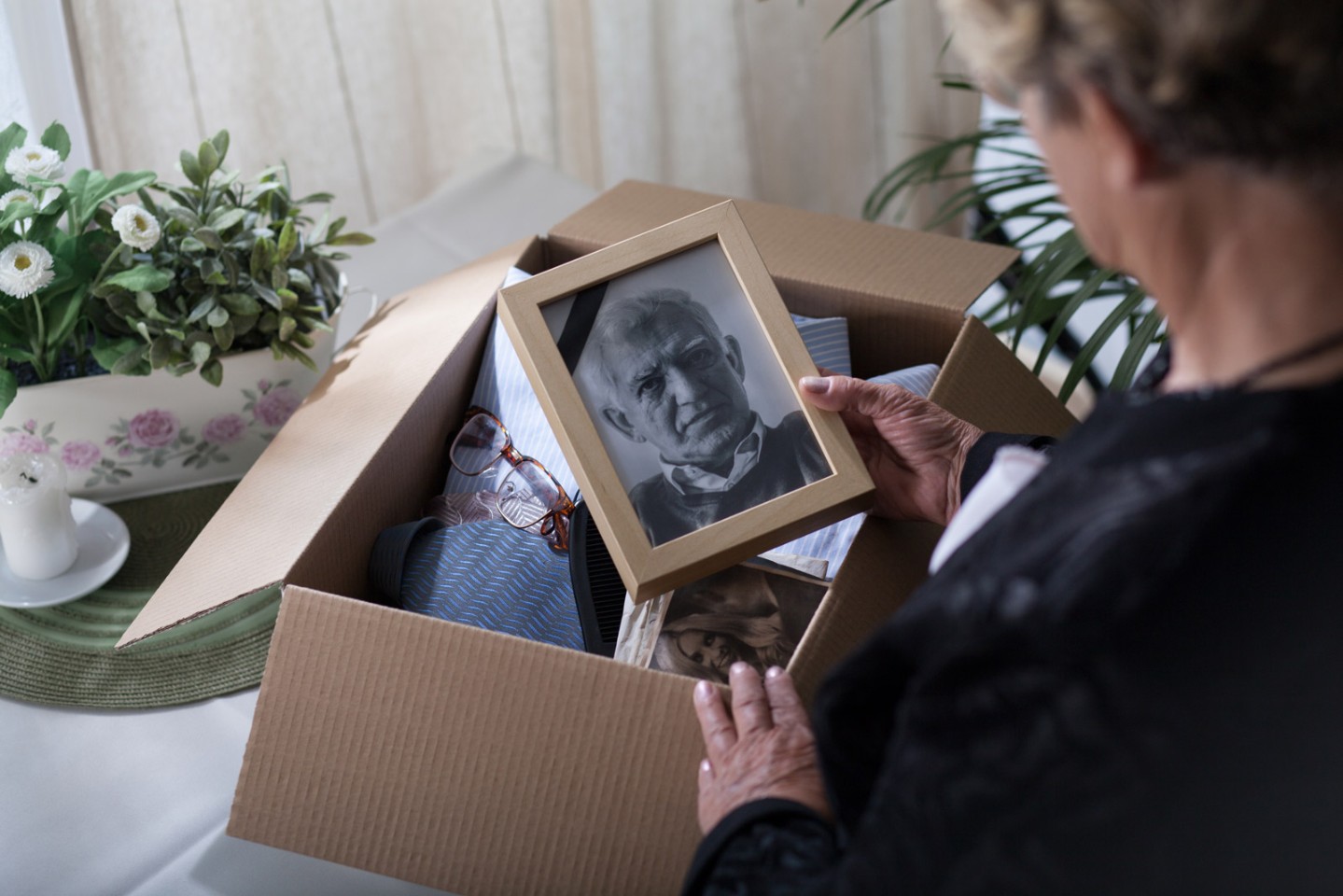 Older woman looking in a box of things and holding a black and white photo of an old man
