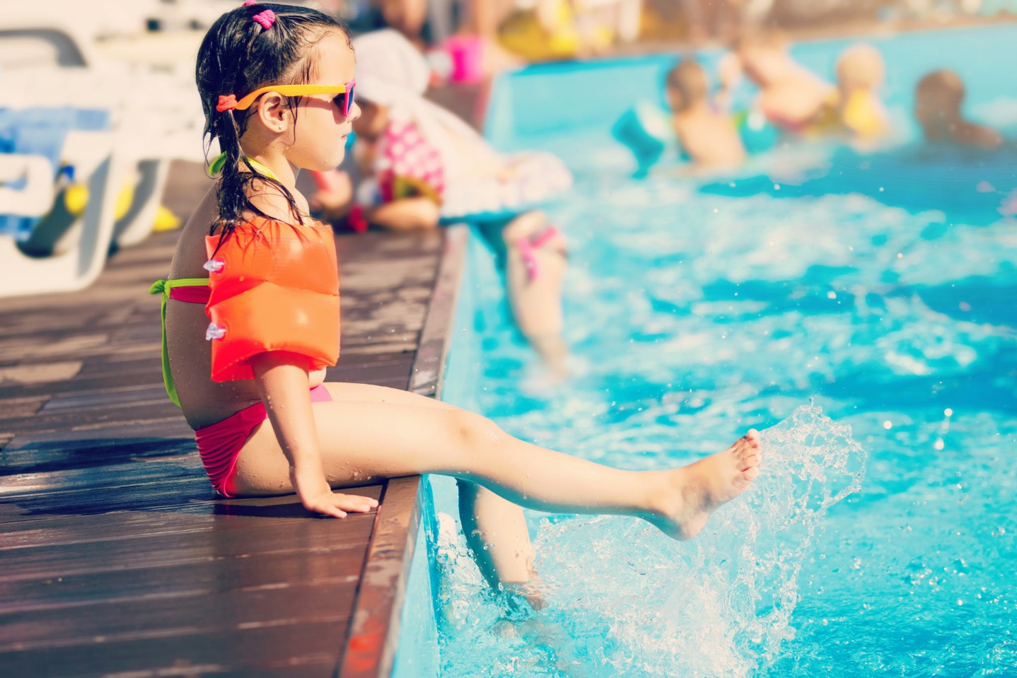 Little girl playing in outdoor swimming pool jumping into water on summer vacation on tropical beach island. Child learning to swim in outdoor pool of luxury resort.