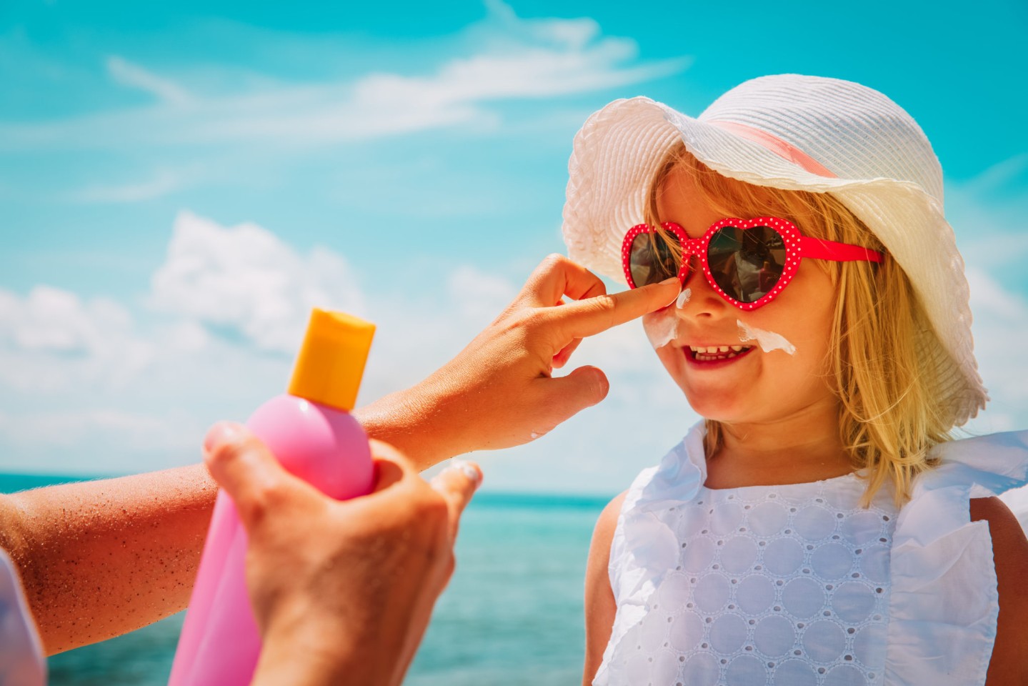 mother putting sunblock cream on little daughter face at beach