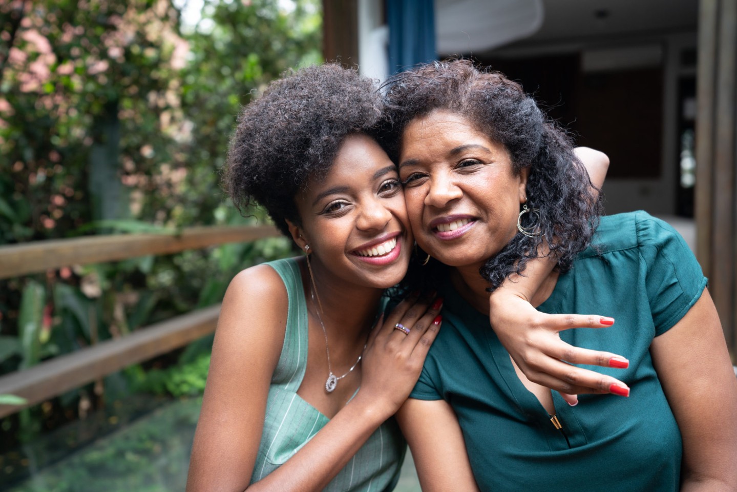 African American Mother and Daughter Embracing outside on a deck, smiling at the camera