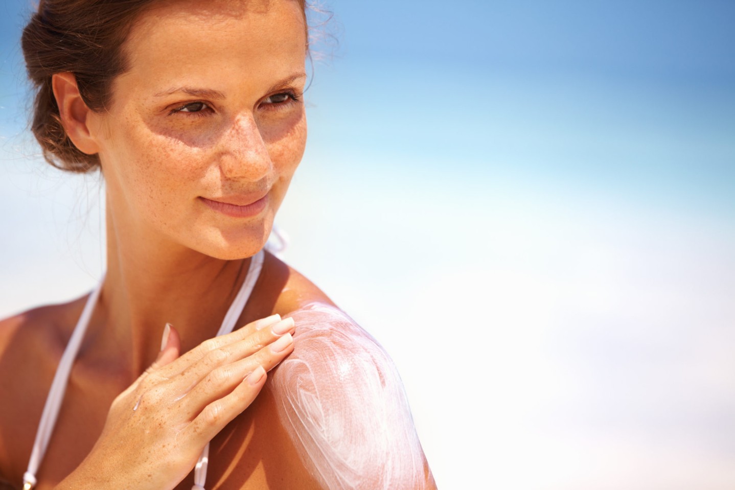 Closeup of lovely young woman applying sunscreen lotion on body