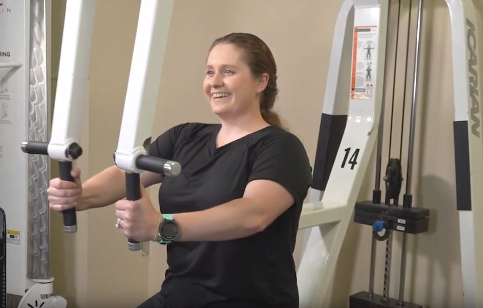 Lady demonstrating how to use a pec fly weight machine