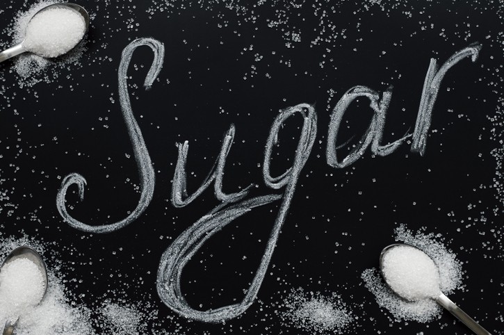 Sugar eating concept. Refined white sugar in small spoons on black background. Food lettering. The word "Sugar"