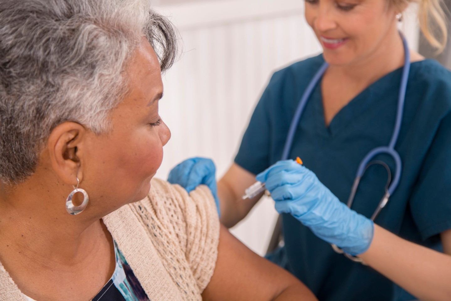 Nurse gives flu vaccine to senior adult patient at clinic.