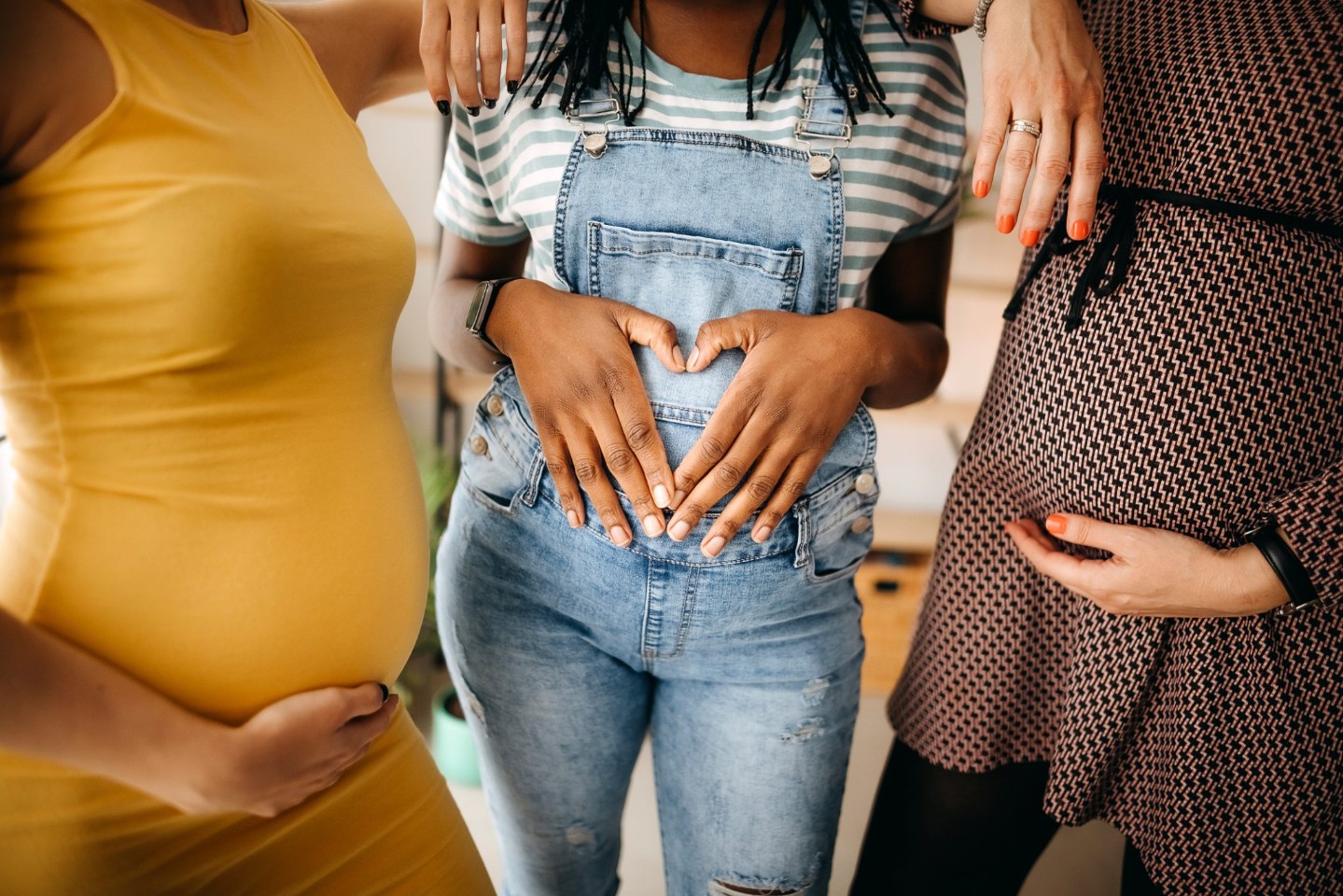 Portrait of three young pregnant women holding their pregnant bellies