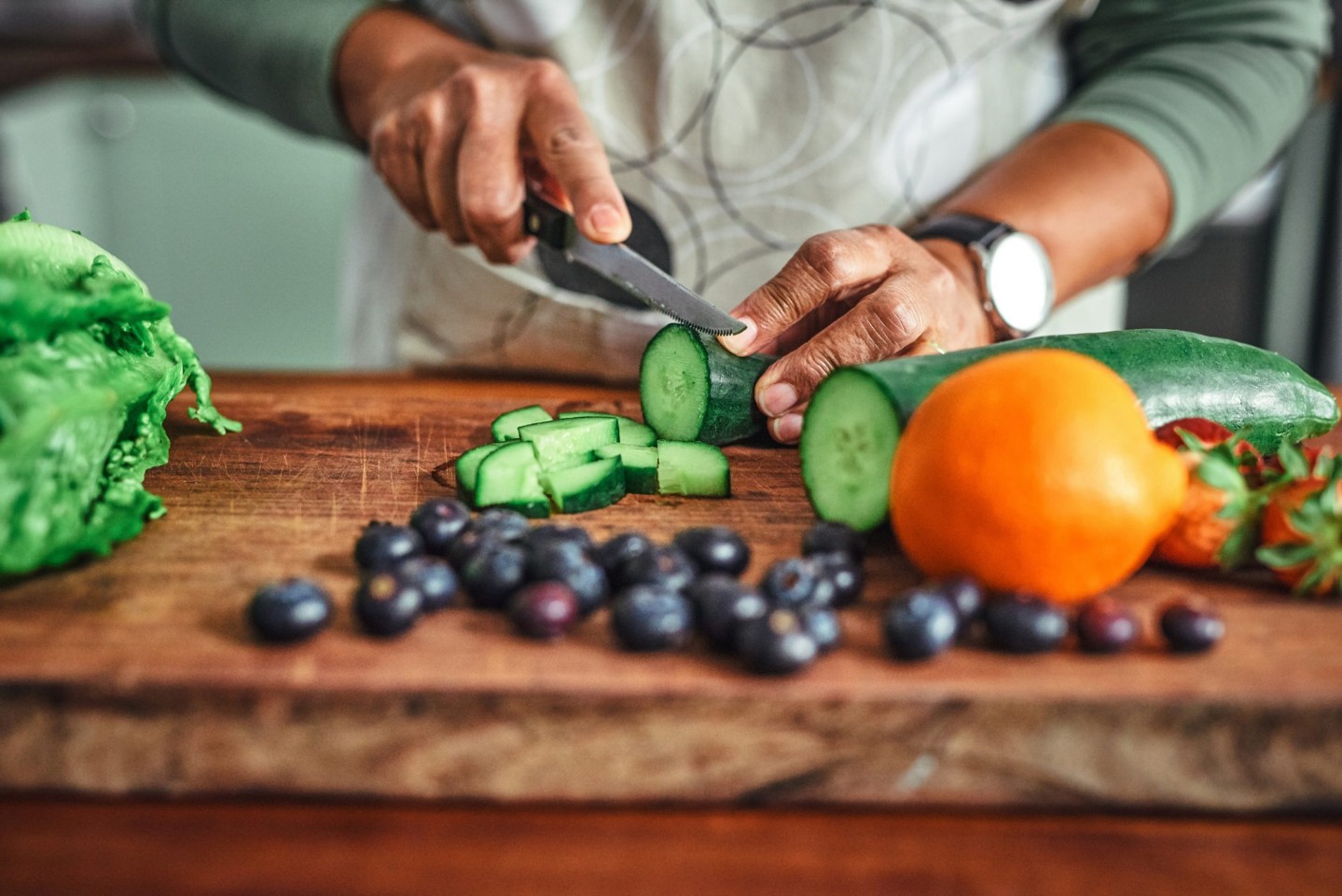 Picture of man cutting vegetables and fruits that can help with cancer prevention like cucumber, oranges, and blueberries.
