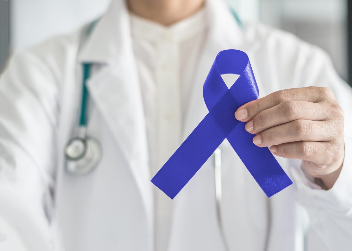 Dark blue ribbon for colon - colorectal cancer awareness on medical doctor's hand support