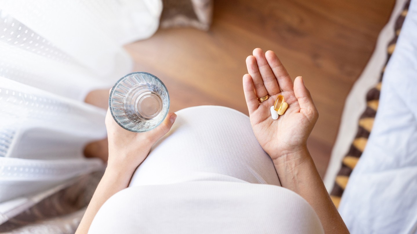 pregnant woman holding a glass and prenatal vitamins