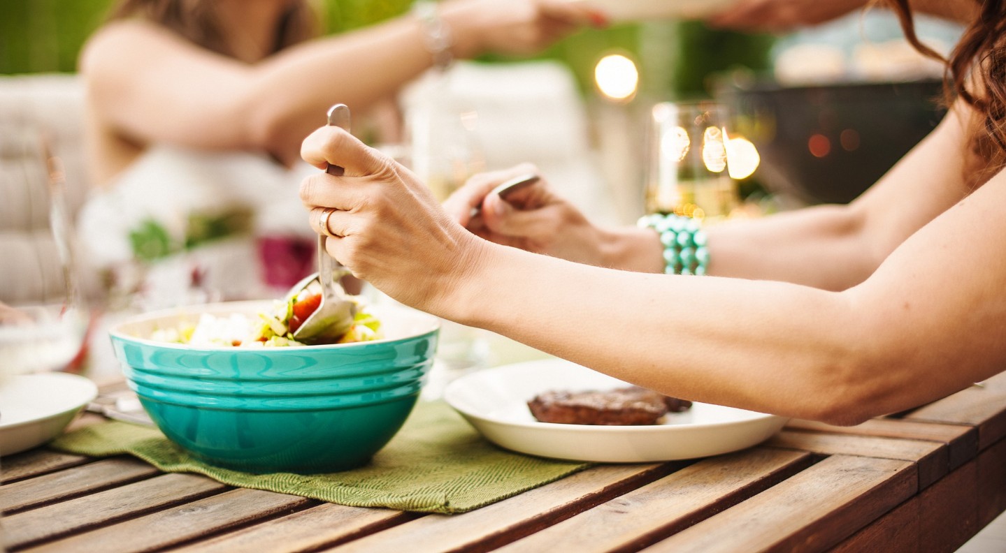 arms reaching to mix a salad at outdoors meal